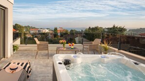 A rooftop terrace with a hot tub, lounge chairs, and a table with flowers.