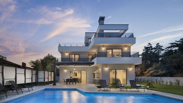 A modern two-story house with a swimming pool, outdoor seating, and a well-lit patio area.