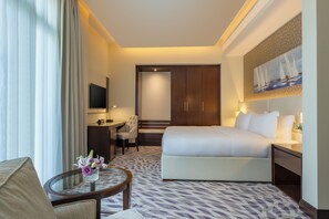 A hotel room with a bed, a desk, a chair, a TV, and a painting on the wall.