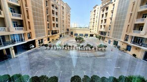 A courtyard with a central roundabout surrounded by potted plants, multiple floors of residential buildings with balconies, and a clear sky.