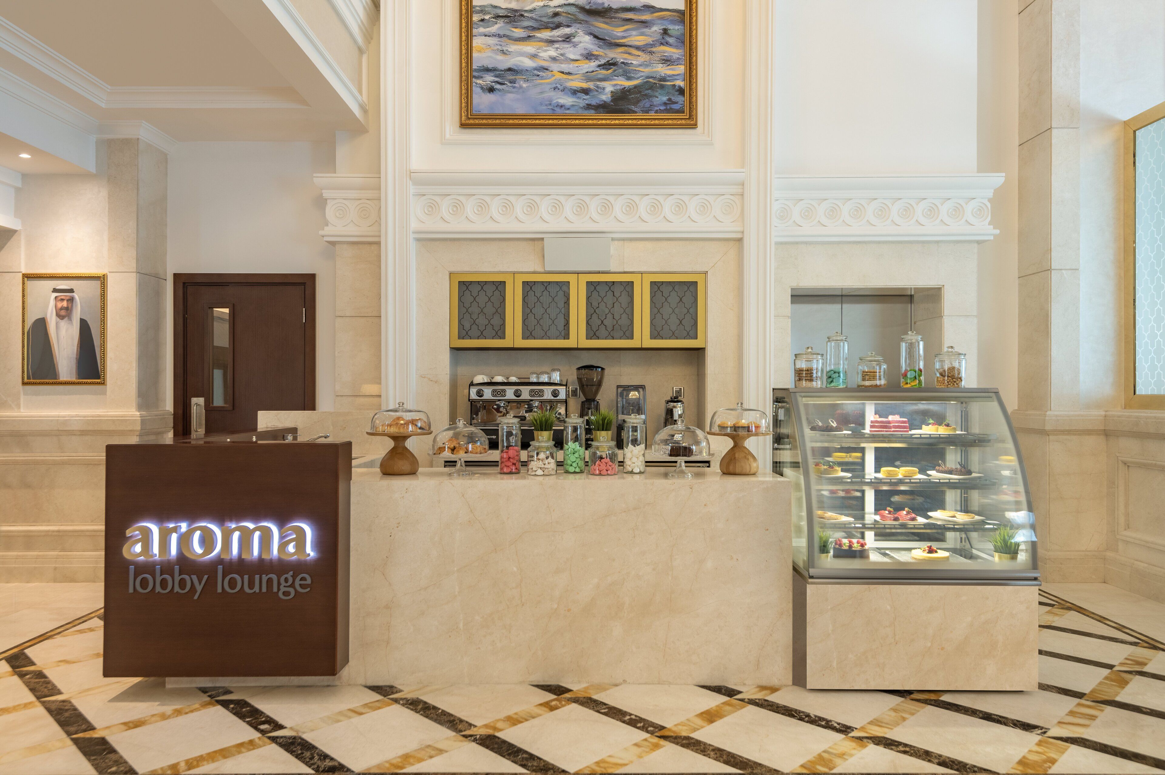 Een lounge in de lobby met een receptiebalie, een vitrine met gebak en een schilderij aan de muur.