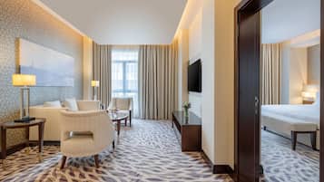 Habitación de hotel con alfombra estampada, un sofá, una silla, una mesita, televisor y cama.