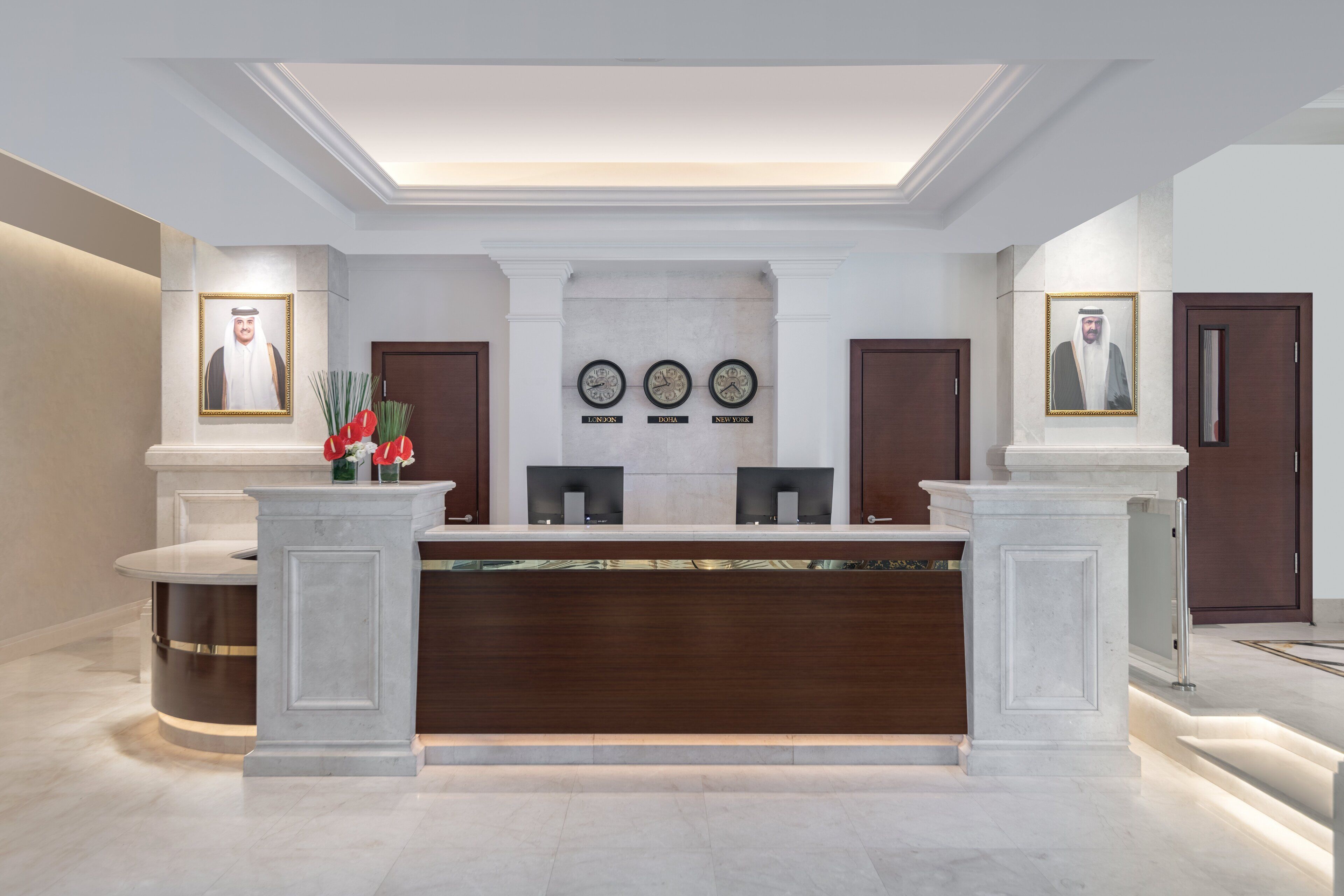 A reception area with a marble counter, framed portraits, clocks, and a modern design.