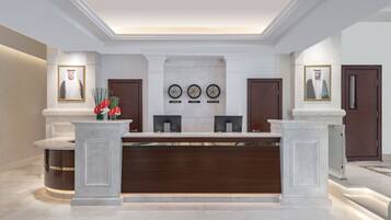 A reception area with a marble counter, framed portraits, clocks, and a modern design.