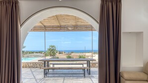 Una stanza con vista sulla piscina e sul mare, una panca di legno e un divano color beige.