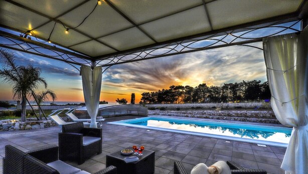 Area piscina all'aperto con lettini, un tavolo con bevande e vista sul tramonto.