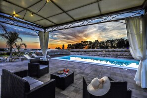 An outdoor pool area with lounge chairs, a table with drinks, and a sunset view. - Large villa (2 apt) with pool & rooftop jacuzzi (Lido Marini)