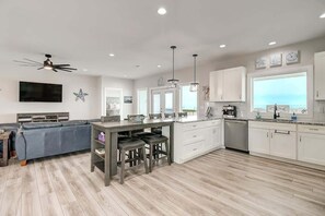 A modern kitchen with a dining area, wooden flooring, white cabinetry, and a large window.