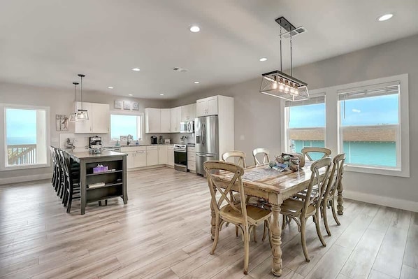 A modern kitchen with white cabinets, a dining area with a wooden table and chairs, and large windows with a view.