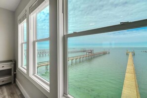 A room with large windows overlooking a wooden pier extending into a calm body of water.