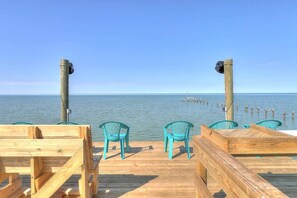 A wooden deck with chairs and tables, overlooking a calm sea with a clear sky.