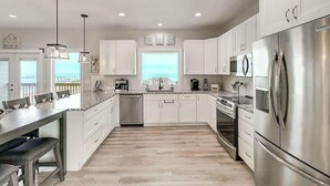 A modern kitchen with white cabinets, stainless steel appliances, and a large island with seating. - Soggy Pollards (Rockport)