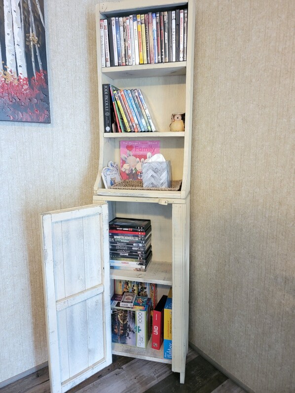 Una pequeña estantería blanca con varios libros y DVDs.