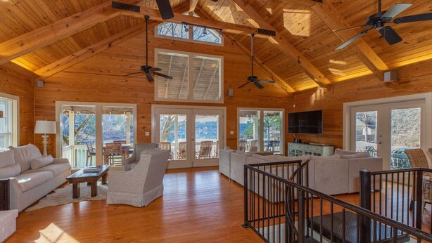 A spacious living room with wooden floors, ceiling fans, and large windows offering views of the outdoors.