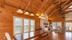 A spacious wooden cabin with a large dining table, multiple windows, and a cozy seating area.