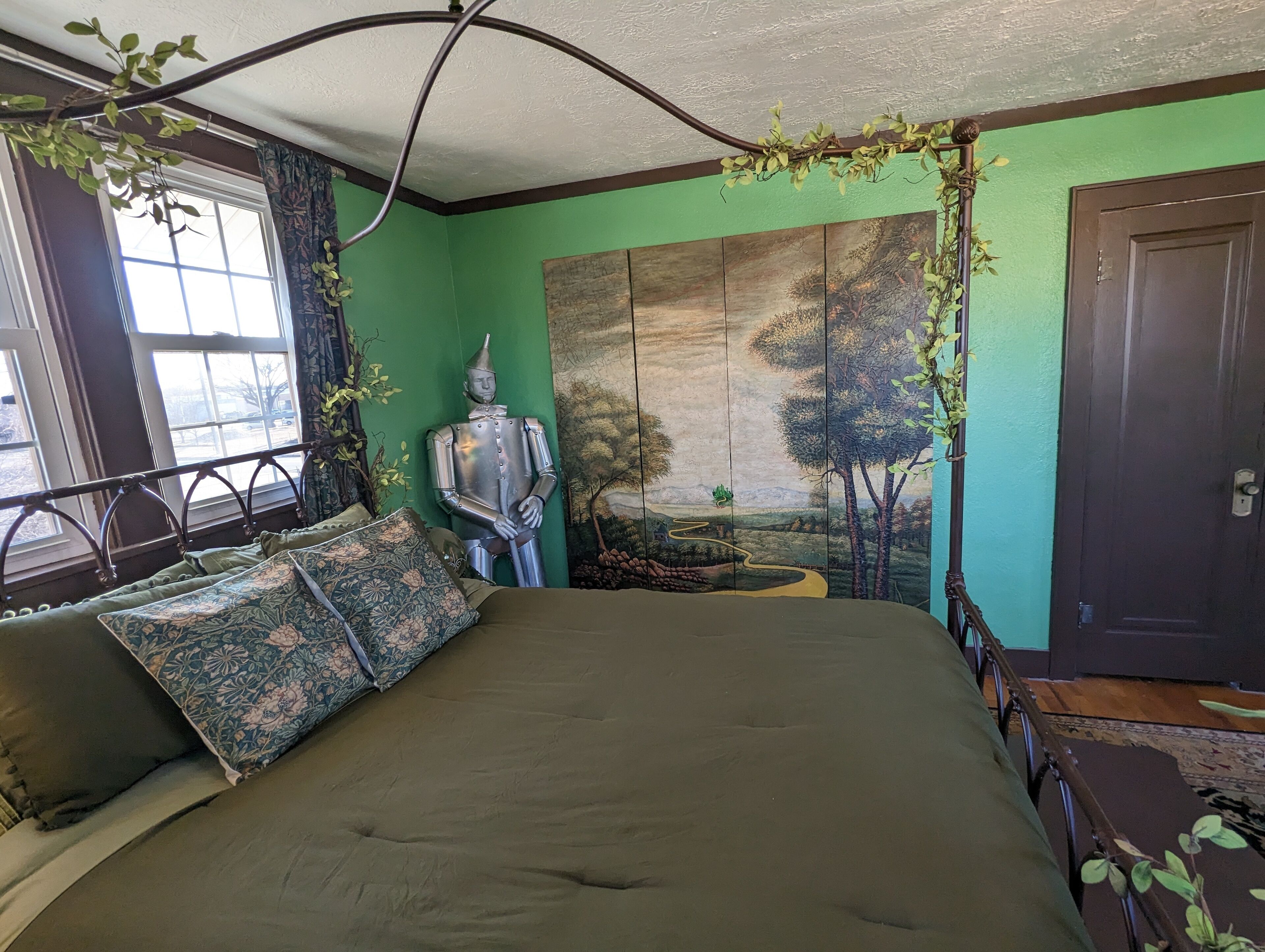 A bedroom with a large bed, a green wall, a painting, and a metal sculpture.