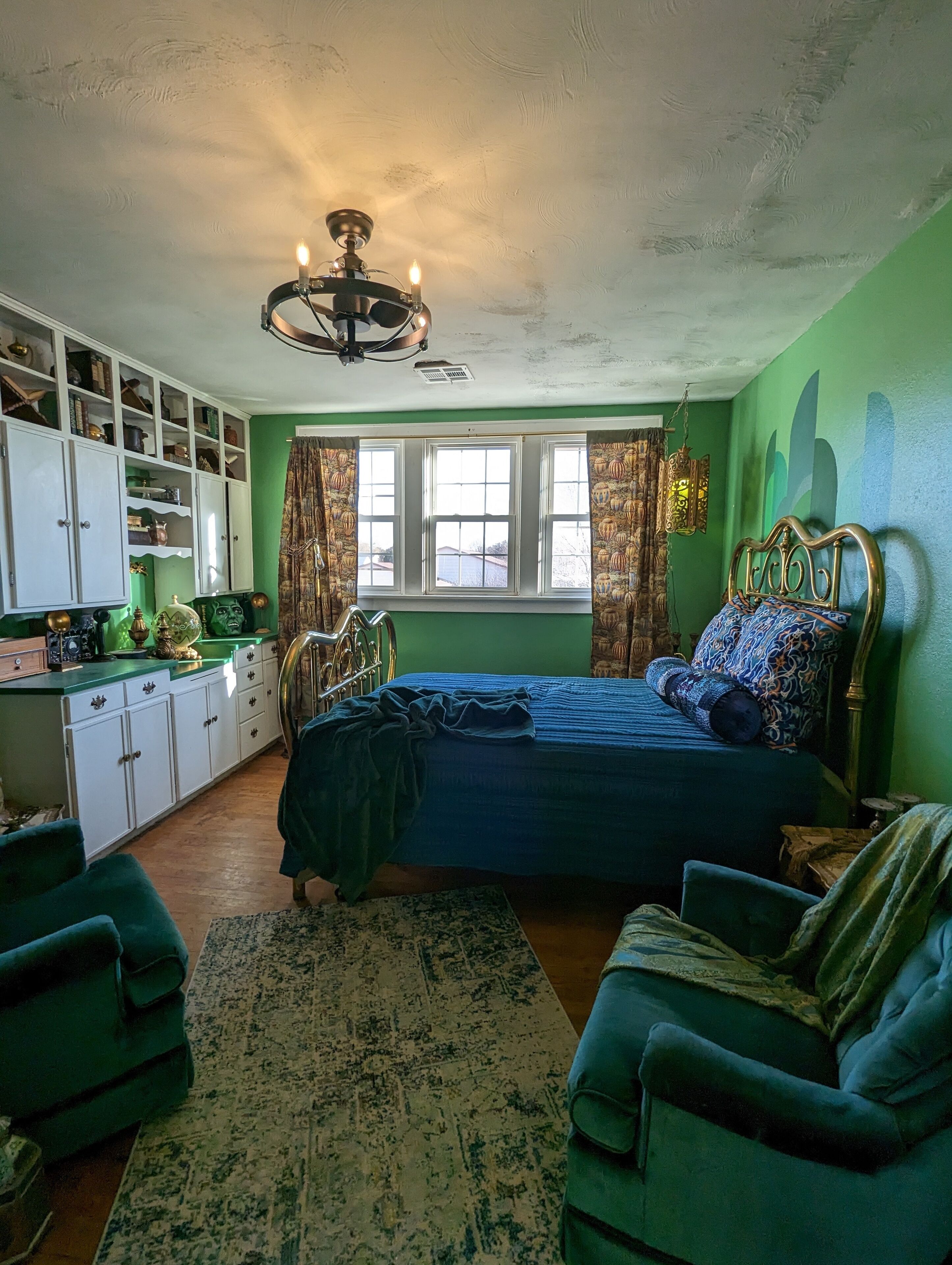 A bedroom with a bed, green walls, a window, a ceiling fan, and a wardrobe.
