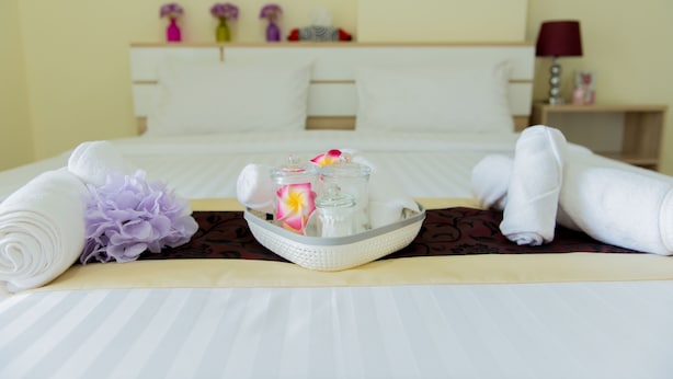 Een net opgemaakt bed met opgerolde handdoeken, een dienblad met toiletartikelen en decoratieve bloemen.
