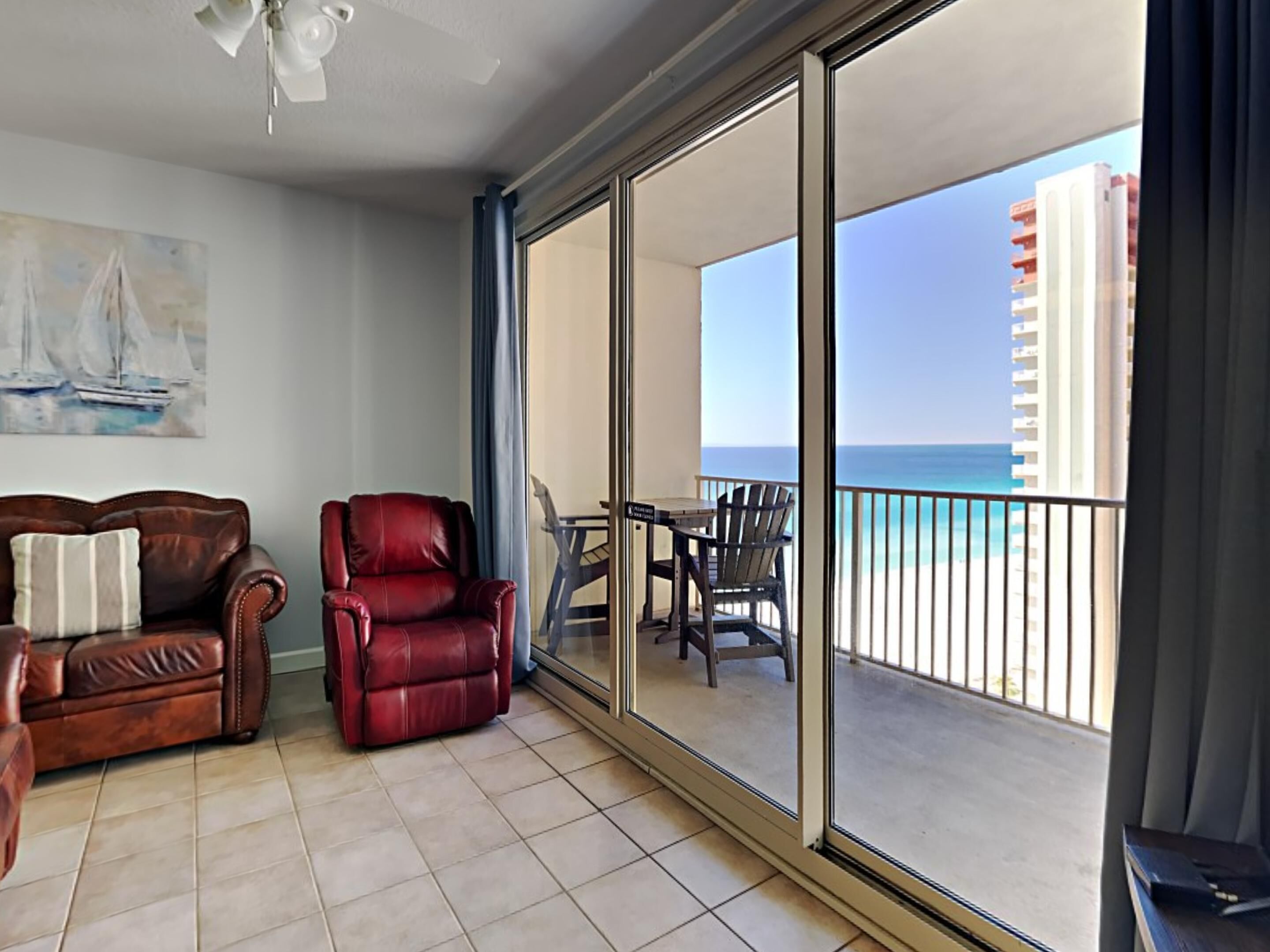 A balcony with a view of the ocean, a leather sofa, a red chair, and a dining table with chairs.