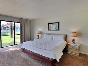 Quarto de hotel com uma cama grande, duas mesas de cabeceira com abajures, uma janela com vista para um edifício e uma área ajardinada, e um quadro pendurado na parede.