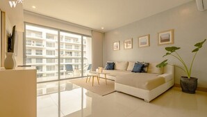 A modern living room with a sofa, a coffee table, and a large window offering a view of a building. - w* | Stunning 1BR with Pool in Cartagena (Cartagena de Indias)