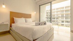 A modern hotel room with a large bed, a wooden headboard, a nightstand, and a balcony with a view of other buildings. - w* | Stunning 1BR with Pool in Cartagena (Cartagena de Indias)