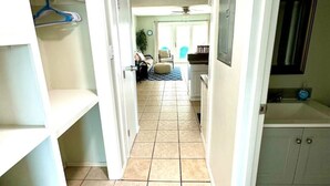 A hallway with a tiled floor, a door leading to a room, and a small seating area with a chair and a table.