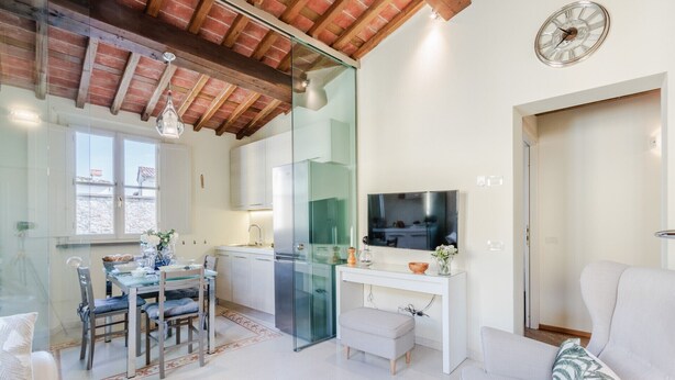 A modern living room with a white sofa, a glass dining table, and a TV on a white console.