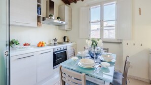 A modern kitchen with white cabinets, a built-in oven, and a dining area with a glass table set for four.