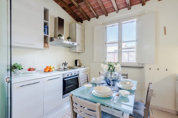 A modern kitchen with white cabinets, a built-in oven, and a dining area with a glass table set for four.