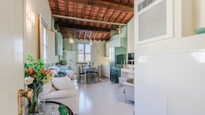 A modern kitchen with a glass door, a dining area with a table and chairs, and a living room with a sofa and decorative plants.