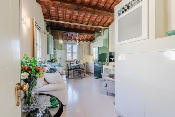 Une cuisine moderne avec une porte en verre, un coin repas avec une table et des chaises, et un salon avec un canapé et des plantes décoratives.