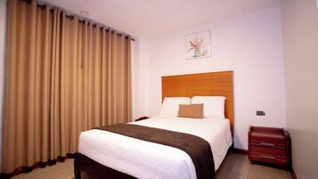 Una habitación de hotel con una cama grande, cabecera de madera, mesita de noche y un cuadro en la pared.
