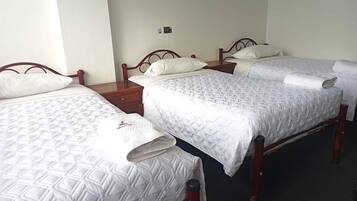Una habitación de hotel con dos camas individuales, cada una con cabecero de madera, ropa de cama blanca y una mesita de noche con lámpara.