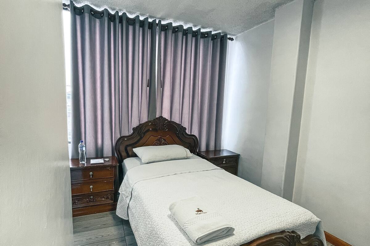 A bedroom with a wooden bed, a nightstand, a dresser, and a window with curtains.