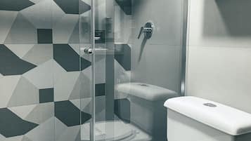 Un baño moderno con un salpicadero de azulejos geométricos, mampara de ducha de vidrio, inodoro y estante de madera con una toalla.