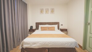 Ein Hotelzimmer mit einem großen Bett, zwei Nachttischen, einem Schreibtisch und einer mit Vorhängen versehenen Tür sowie einem Fenster.