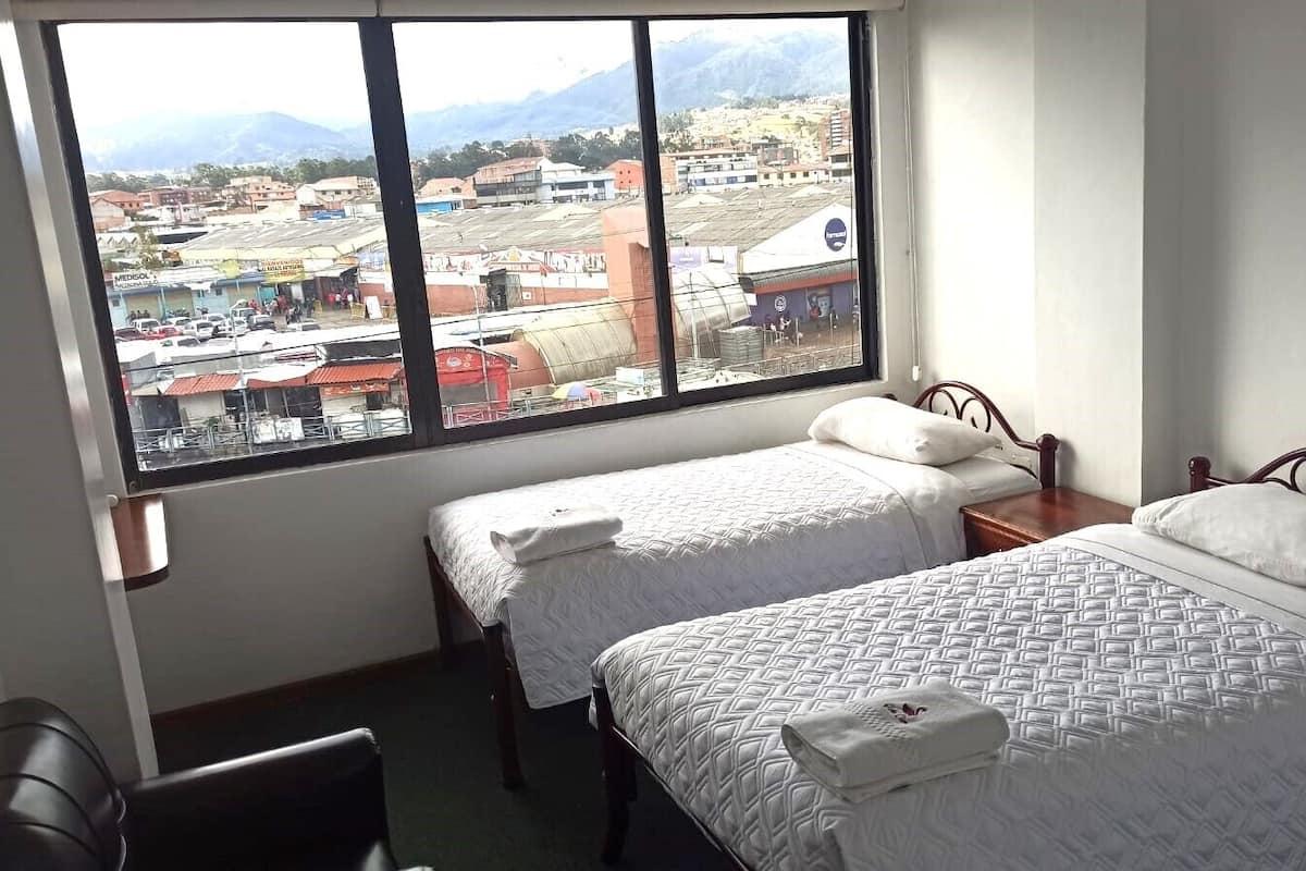 A hotel room with two beds, a window with a view of a cityscape and mountains, and a chair.