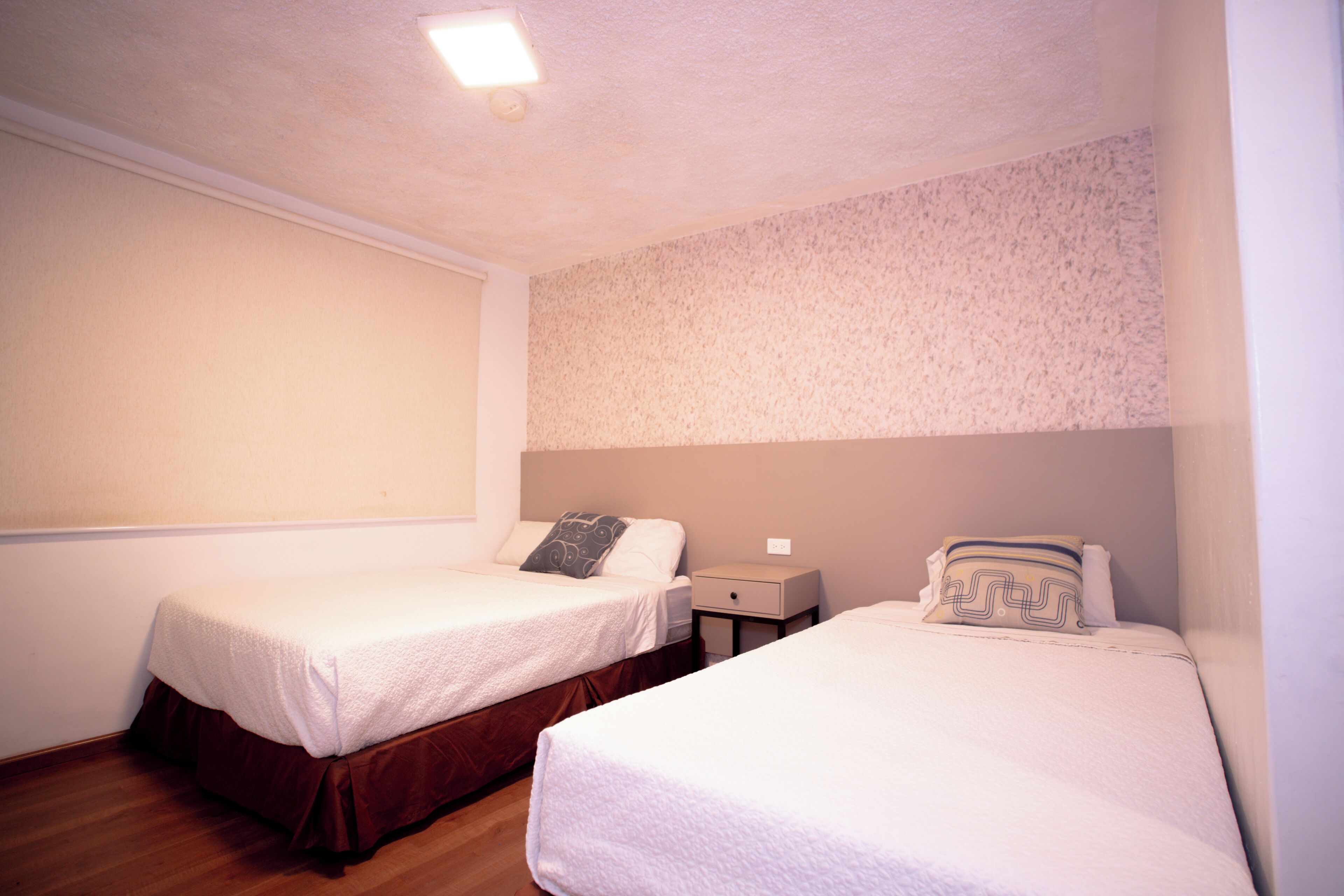 A room with two single beds, a nightstand, and a wall-mounted light fixture.