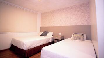 A room with two single beds, a nightstand, and a wall-mounted light fixture.