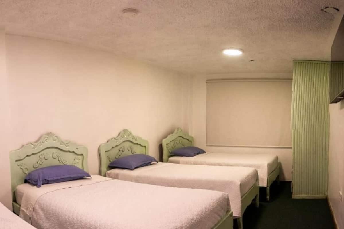 A room with three single beds, each with a headboard and a pillow.