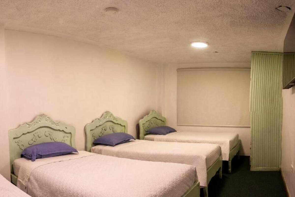 A room with three single beds, each with a headboard and a pillow.