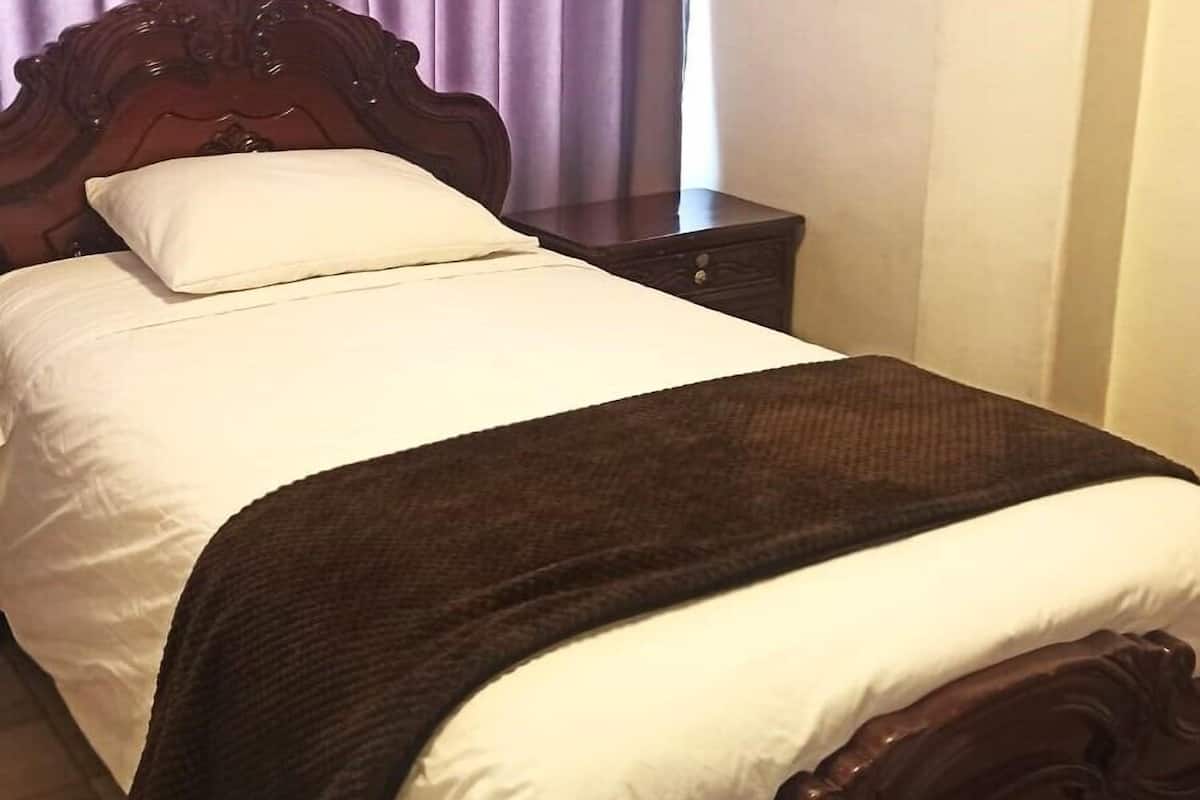 A bed with a wooden headboard, white bedding, and a brown throw blanket.
