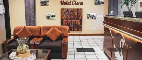 A hotel lobby with a reception desk, a sofa with cushions, a coffee table with a vase, and framed pictures on the wall.