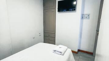 A hotel room with a single bed, a television mounted on the wall, and a door leading to another room.