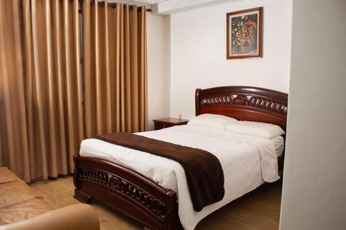 A bedroom with a wooden bed, a nightstand, a chair, and a painting on the wall.