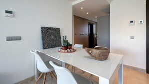 Un espace repas moderne avec une table blanche, deux chaises blanches, un cactus en guise de centre de table et un bol en bois.