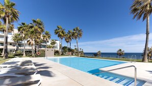 Une piscine avec des chaises longues, des palmiers et une vue sur l’océan.