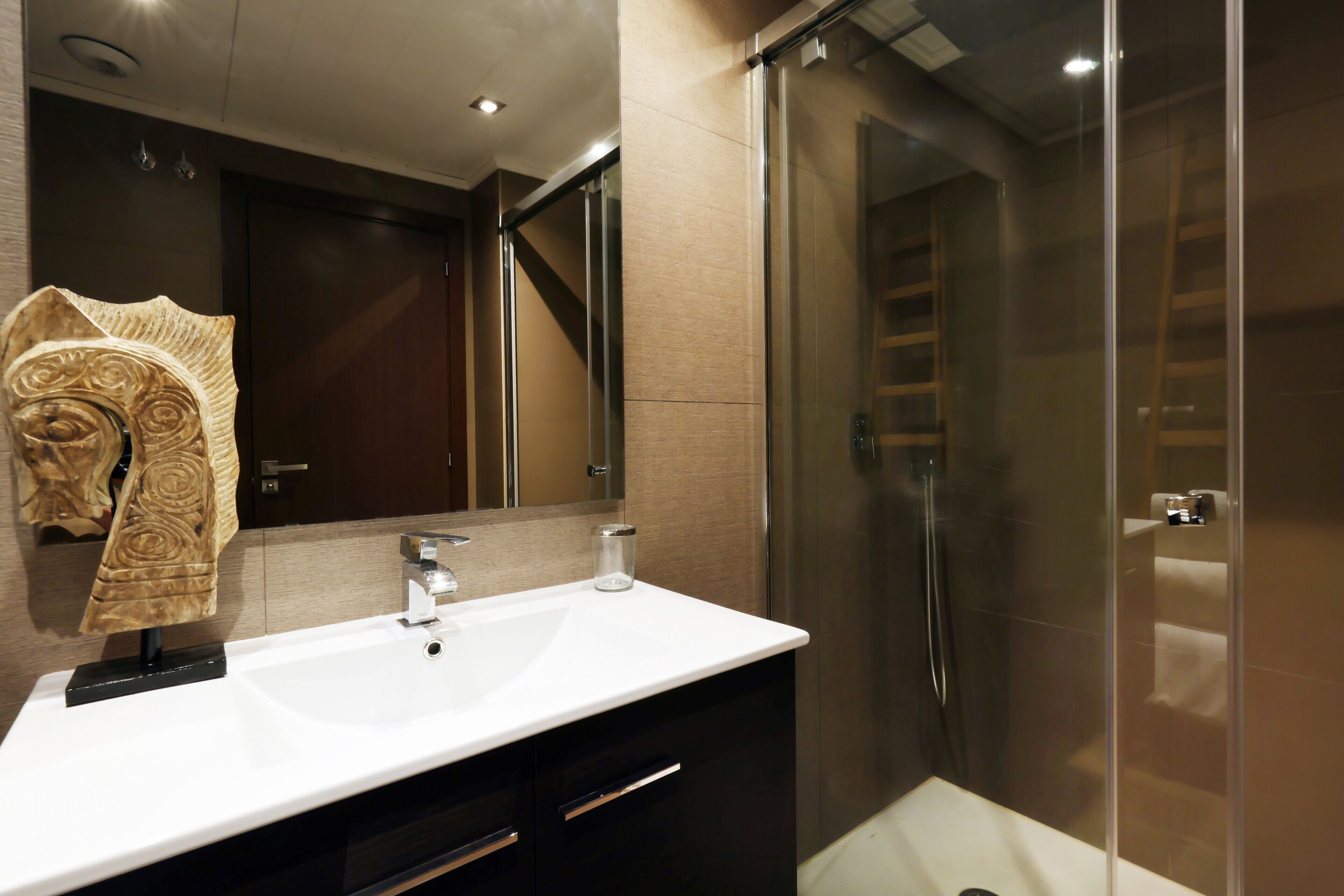 Un baño moderno con lavamanos blanco, cabina de ducha de vidrio y mueble de tocador de madera oscura.