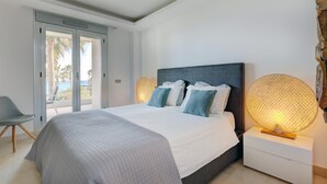 Une chambre à coucher avec un lit, des tables de chevet, une chaise et une vue sur l’extérieur, accessible par une porte coulissante.